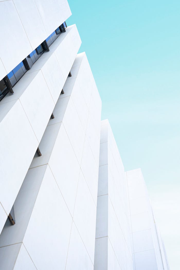 Low angle shot of a modern white facade showcasing minimalist architecture against a bright blue sky.